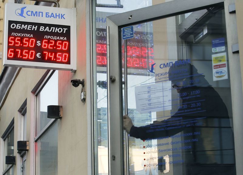 © Reuters. A man walks out of a bank office, with an electronic board showing currency exchange rates seen above, in central Moscow
