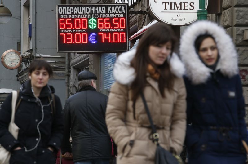 © Reuters. People walk past a board showing currency exchange rates in Moscow