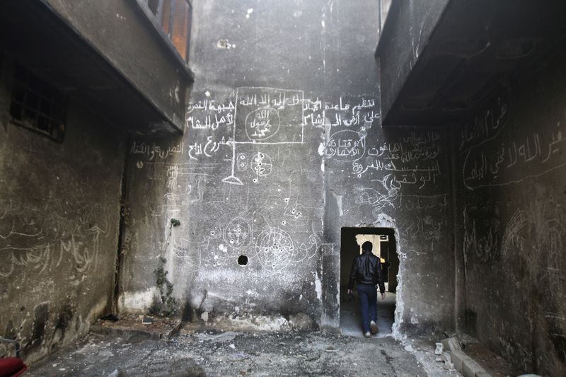 © Reuters. A man walks inside a damaged building with an Islamic flag drawn on the wall in the besieged town of Arbeen in the eastern Ghouta of Damascus