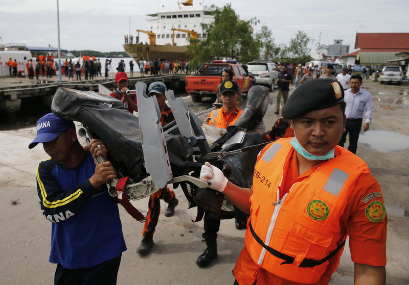 © Reuters. Rescue team members walk as they carry the wreckage of a seat of the AirAsia Flight QZ8501 airliner at Kumai port