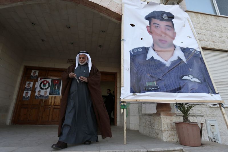 © Reuters. A relative of Islamic State captive Jordanian pilot Muath al-Kasaesbeh walks past a poster of Muath in front of his clan's headquarters in Amman