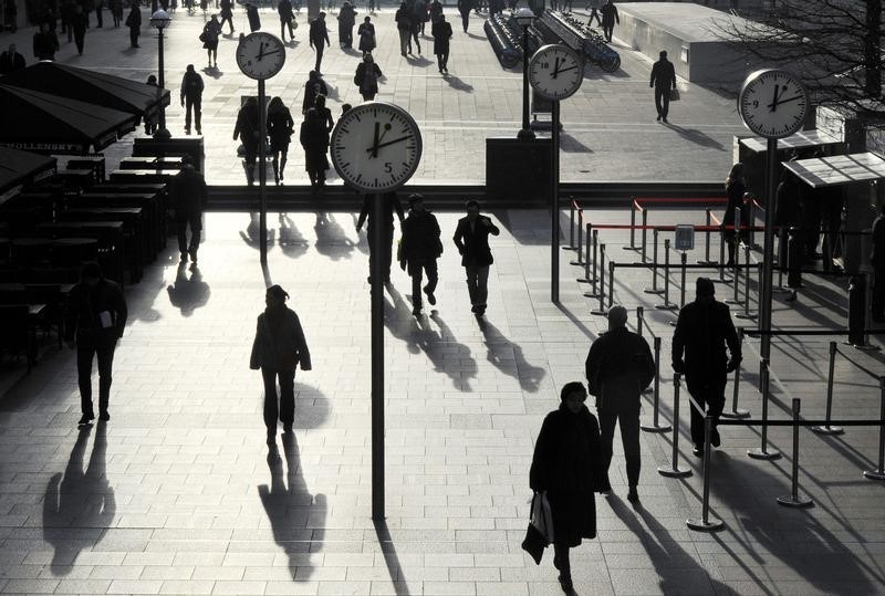 © Reuters. Workers walk past clocks showing a time of 12 minutes past 12 noon, on this century's last sequential date, in a plaza in the Canary Wharf business district of London