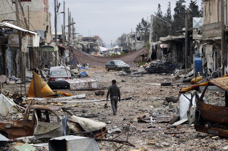 © Reuters. A man walks in a street with abandoned vehicles and damaged buildings in the northern Syrian town of Kobani