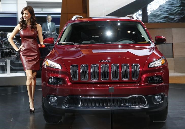 © Reuters. A model poses next to a Jeep Cherokee during the press preview day of the North American International Auto Show in Detroit