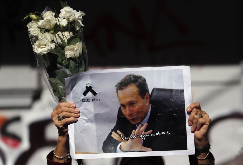 © Reuters. A woman holds up flowers and an image of late prosecutor Alberto Nisman while waiting for the hearse with his remains, in Buenos Aires