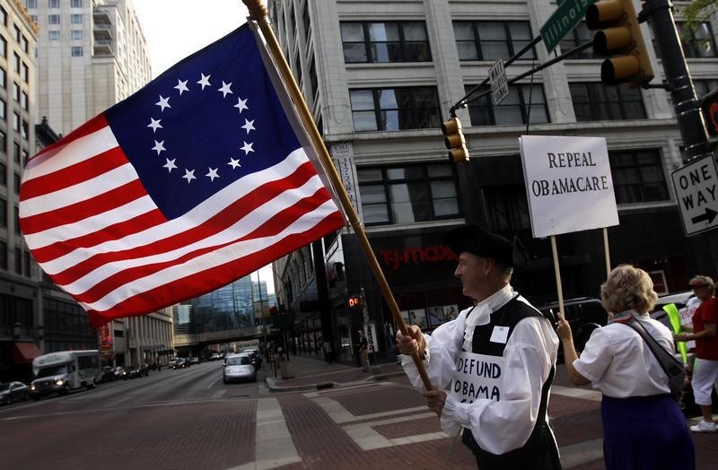 © Reuters. Wheeler waves a flag while standing with a small group of demonstrators outside of the HIlton Hotel and Suites prior to a "Defund Obamacare Tour" rally in Indianapolis