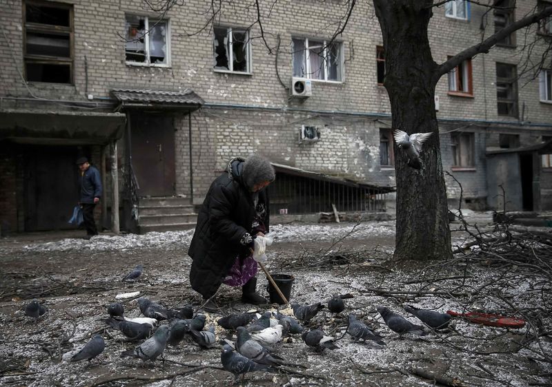 © Reuters. Mulher alimenta pombos diante de casa destruída em Debaltseve