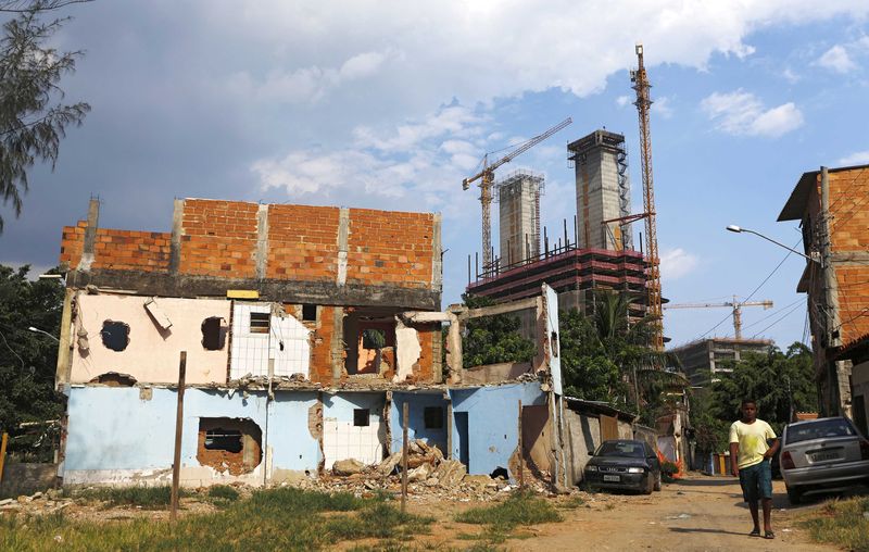 © Reuters. A boy walks past a partially demolished house, with cranes and construction work for the Rio 2016 Olympic Park seen in the background, at the Vila Autodromo favela in Rio de Janeiro