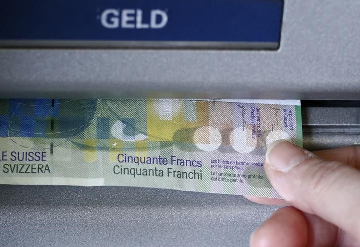 © Reuters. A woman receives several 50 Swiss franc bank note from an ATM in this illustration picture taken in Bern