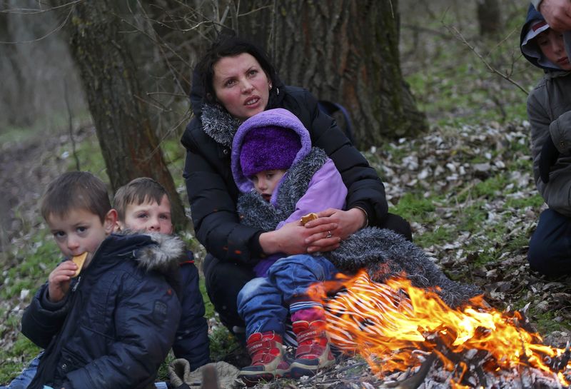 © Reuters. A Kosovar woman holds her child as they warm up around an open fire after they crossed illegally the Hungarian-Serbian border near the village of Asotthalom