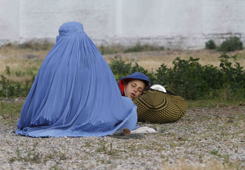© Reuters. An Afghan refugee woman sits with her sleeping boy as they wait with others to be repatriated to Afghanistan, at the United Nations High Commissioner for Refugees (UNHCR) office on the outskirts of Peshawar