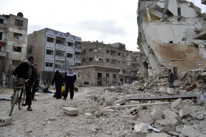 © Reuters. Residents walk past damaged buildings after what activists said were air strikes by forces loyal to Syria's President Bashar al-Assad in the Douma neighborhood of Damascus