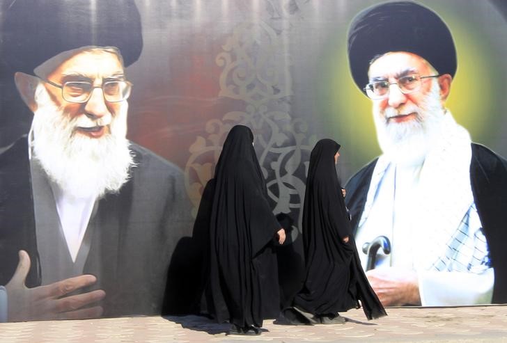 © Reuters. Iraqi women walk past a poster depicting images of Shi'ite Iran's Supreme Leader Ayatollah Ali Khamenei at al-Firdous Square in Baghdad