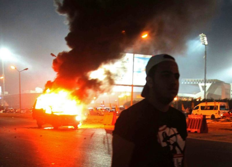 © Reuters. A soccer fan is seen near a police car, which was set on fire by fireworks, during clashes between in front of a stadium on the outskirts of Cairo