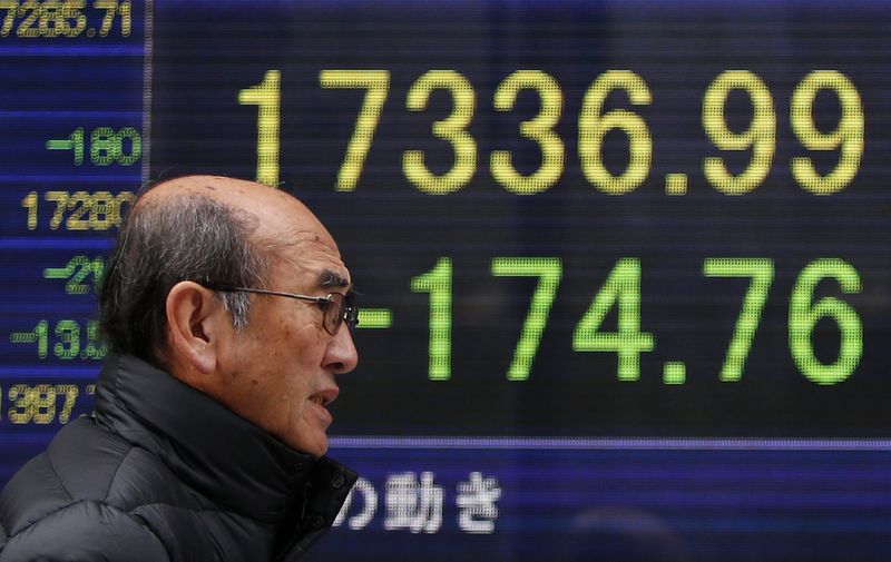 © Reuters. A man walks past an electronic board showing Japan's Nikkei average outside a brokerage in Tokyo