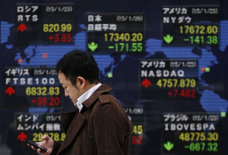 © Reuters. A man holding his mobile phone walks past an electronic board showing the stock market indices of various countries outside a brokerage in Tokyo