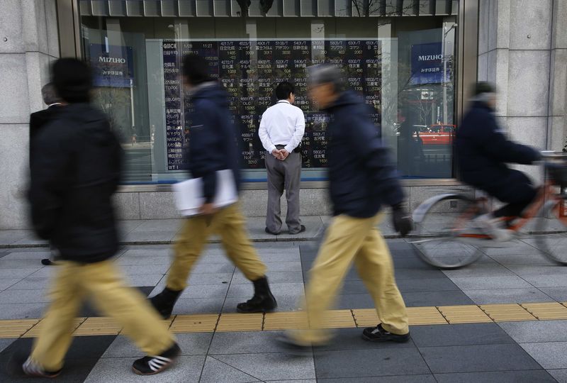 © Reuters. File photo of a man looking at a stock quotation board as passers-by walk past outside a brokerage in Tokyo