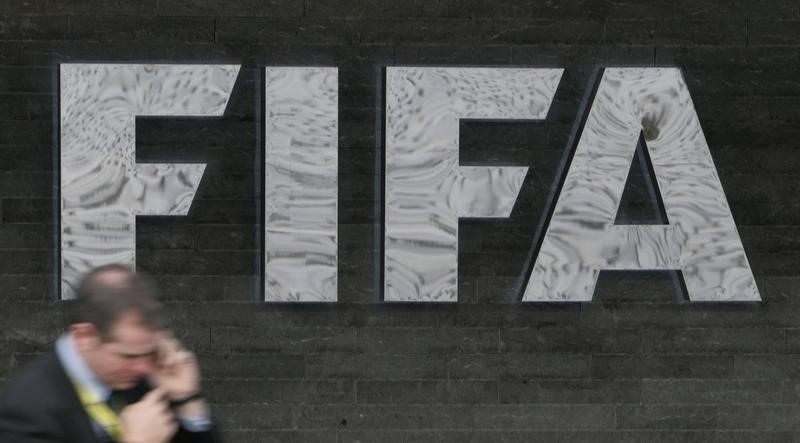 © Reuters. A reporter uses his cell phone as he walks past a FIFA logo in Zurich