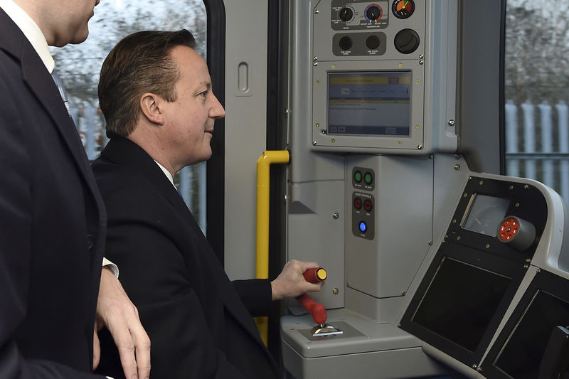 © Reuters. Britain's Prime Minister David Cameron drives a new London underground train as Chancellor of the Exchequer George Osborne looks on during a visit to Bombardier Transportation in Derby