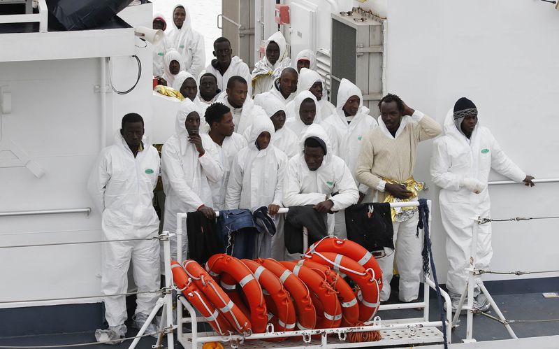 © Reuters. Migrantes están de pie en la cubierta de la nave "Fiorillo" de la guardia costera en su llegada a Porto Empedocle