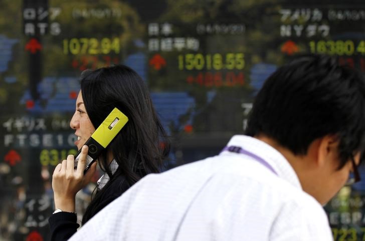 © Reuters. A pedestrian holding her mobile phone walks past an electronic board showing the stock market indices of various countries outside a brokerage in Tokyo