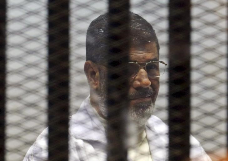 © Reuters. Former Egyptian President Mohamed Mursi sits behind bars with other Muslim Brotherhood members at a court in the outskirts of Cairo