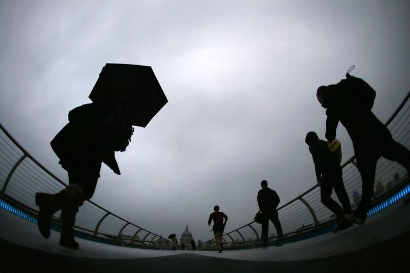 © Reuters. Commuters cross the Millennium Bridge druing a rainy morning in London