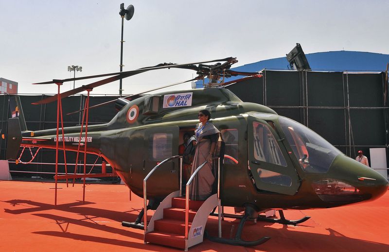 © Reuters. Woman poses for a photograph next to an Indian Air Force light utility helicopter on display at the Aero India air show at Yelahanka air base in Bengaluru