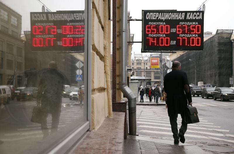 © Reuters. Man walks under a board displaying currency exchange rates in Moscow