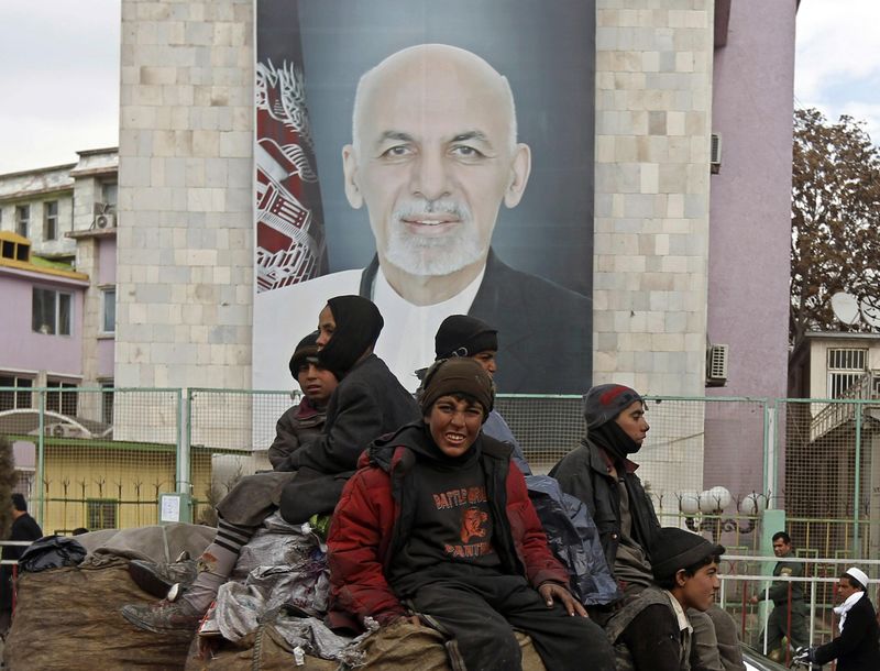 © Reuters. Afghan youths sit on the roof of a car as they pass a picture of Afghan President Ashraf Ghani on a street in Kabul