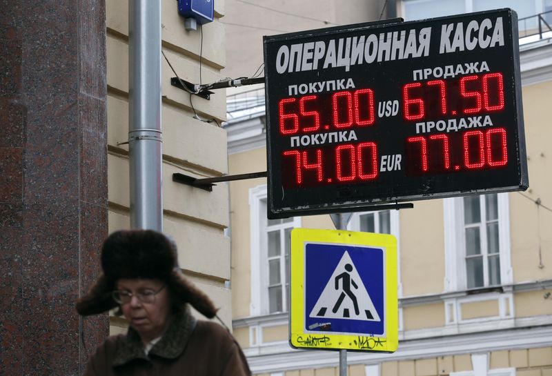© Reuters. Woman walks near a board displaying currency exchange rates in Moscow