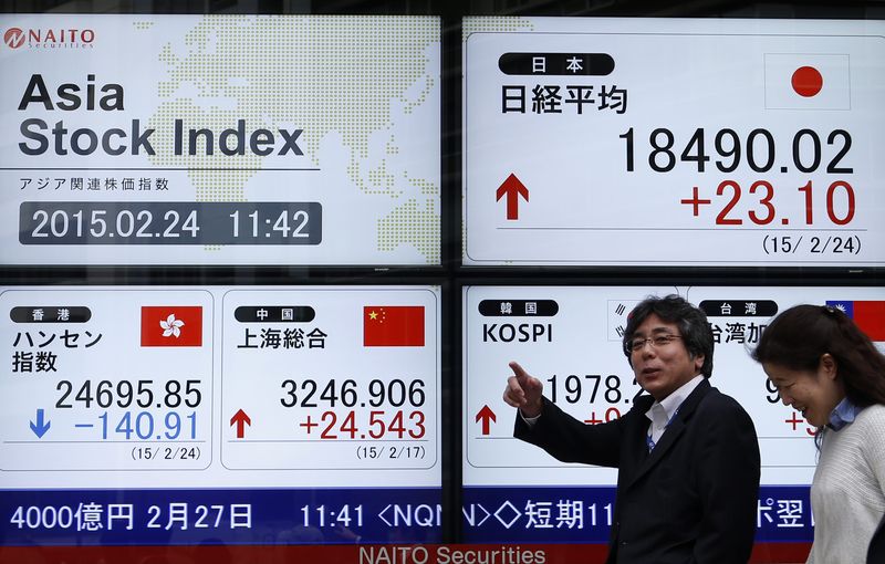 © Reuters. Pedestrians walk past an electronic board showing the stock market indices of various Asian countries outside a brokerage in Tokyo