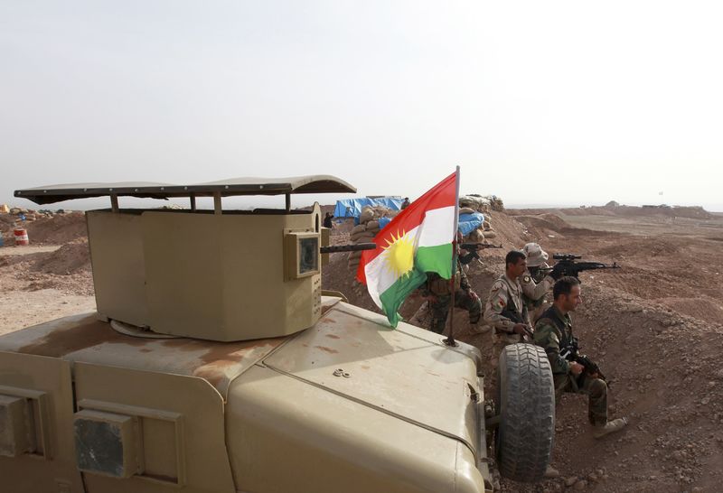 © Reuters. A Kurdish flag is seen next to Peshmerga fighters taking position with their weapons on the frontline against the Islamic State, on the outskirts of Mosul