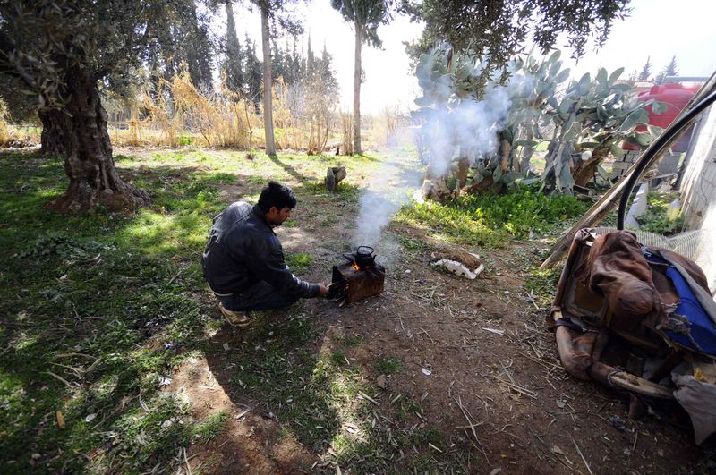 © Reuters. A man starts a fire to prepare tea in Jdeidet Artouz, a suburb of Damascus