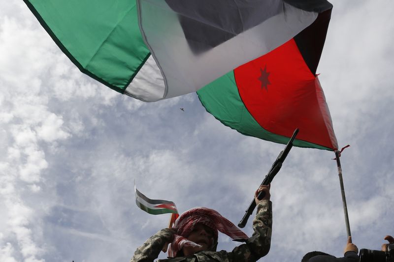 © Reuters. A boy holds a toy gun beside the Jordanian national flag during a march after Friday prayers in Amman