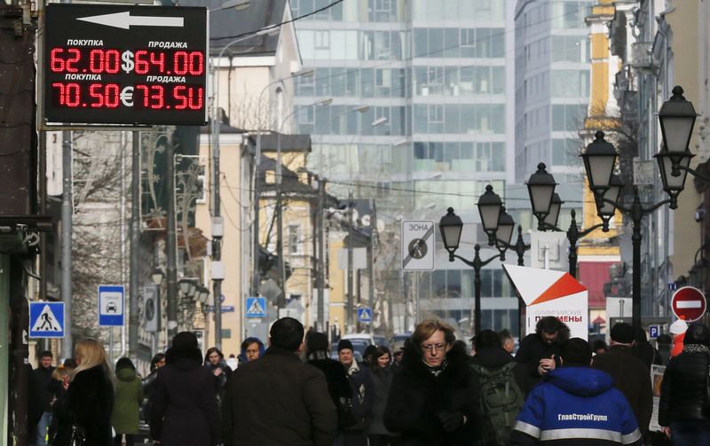 © Reuters. People walk along a street, with a board displaying currency exchange rates seen above, in Moscow