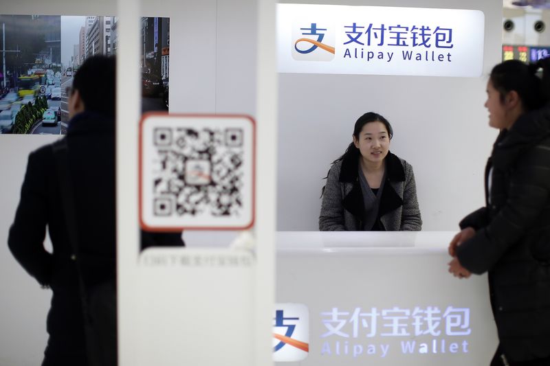 © Reuters. Sales assistant sits behind and under Alipay logos at a train station in Shanghai