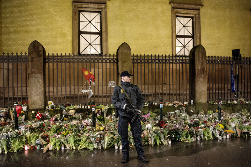 © Reuters. Guard stands in front of bouquets of flowers left as memorials outside a Jewish synagogue during a memorial service for security guard Dan Uzan and film maker Finn Noergaard, who were killed during shooting attacks last week, in Copenhagen