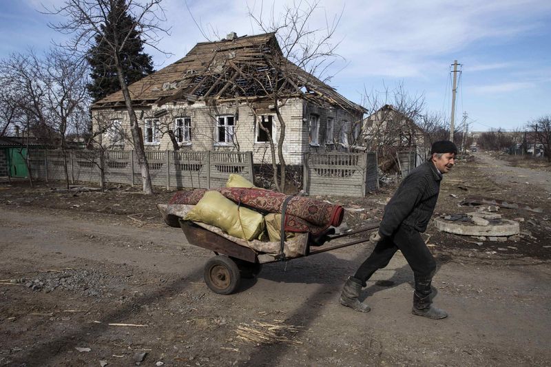 © Reuters. A man pushes a wheelbarrow past a house damaged by fighting in the town of Debaltseve