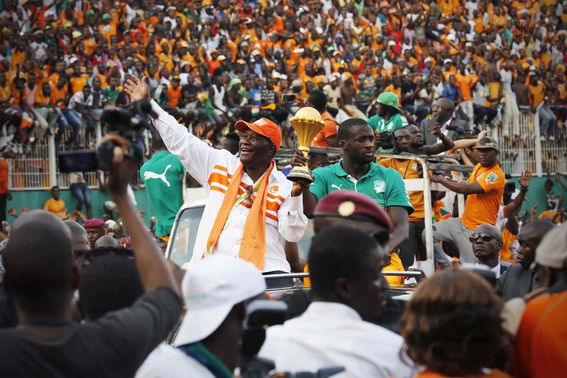 © Reuters. Ivory Coast's President Alassane Ouattara waves as he holds the African Nations Cup trophy with Ivory Coast's soccer team captain Yaya Toure, at the Felix Houphouet-Boigny stadium in Abidjan