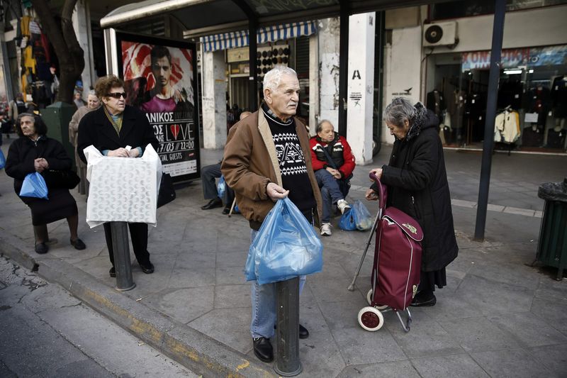 © Reuters. People carrying goods wait at a bus stop in Athens' commercial district