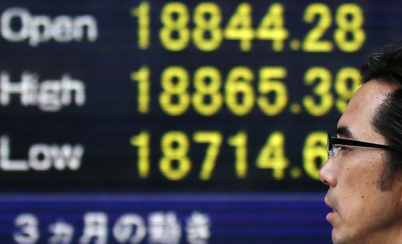 © Reuters. A man walks past an electronic board showing Japan's Nikkei averages outside a brokerage in Tokyo