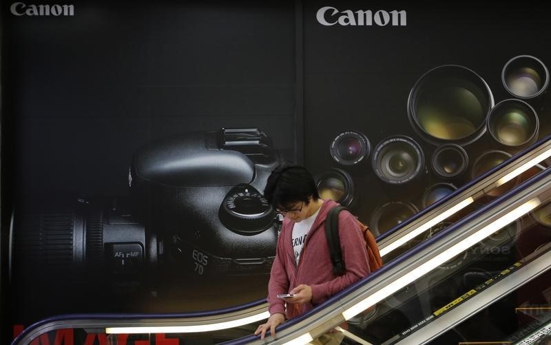 © Reuters. Man rides an escalator past an advertisement for Canon digital camera at an electronics retail store in Tokyo