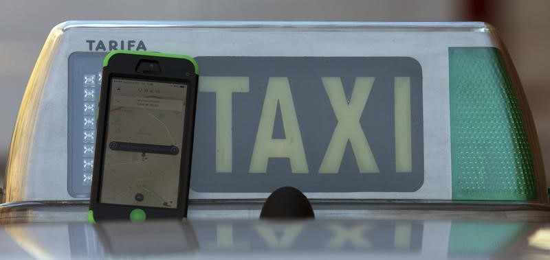 © Reuters. Photo illustration of car-sharing service app Uber on a smartphone next to a taxi sign in Madrid