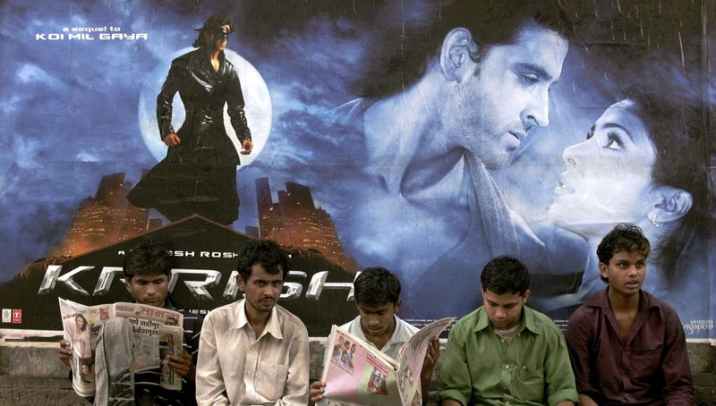 © Reuters. File photo of pedestrians sitting in front of a poster of the upcoming Bollywood film "Krrish" in Mumbai