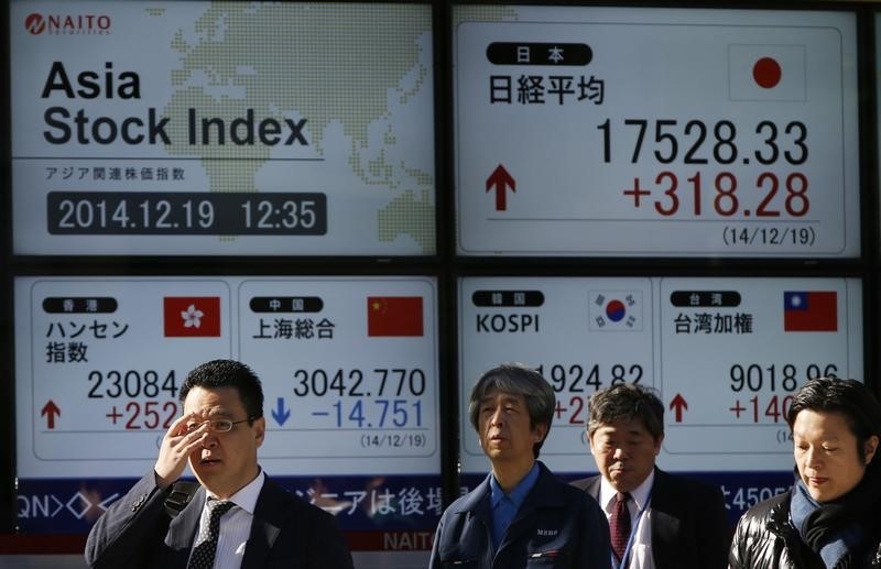 © Reuters. Passersby walk past an electronic board showing Japan's Nikkei share average and Asian countries' stock indexes outside a brokerage in Tokyo