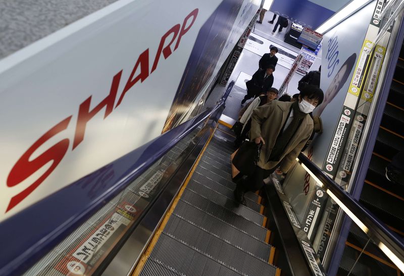 © Reuters. Shopper wearing a mask rides an escalator past advertisements for Sharp Corp's Aquos television at an electronics shop in Tokyo