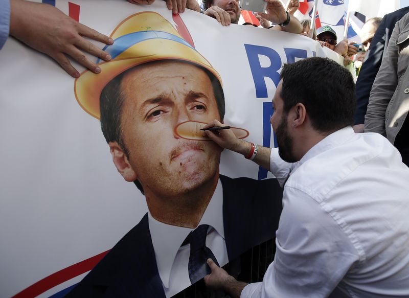 © Reuters. Il leader della Lega Matteo Salvini disegna su uno striscione che ritrae il premier Matteo Renzi durante una manifestazione a Roma