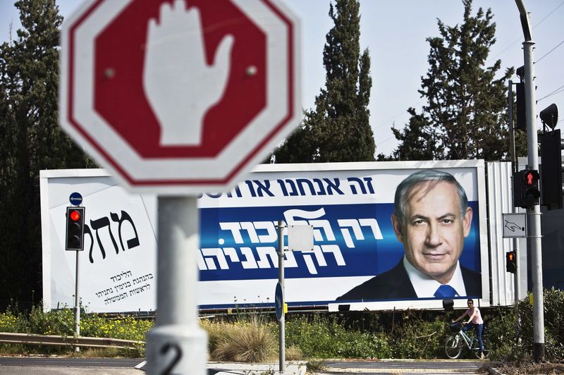 © Reuters. A cyclist rests beside a Likud campaign billboard, depicting Israel's Prime Minister Benjamin Netanyahu, in Tel Aviv