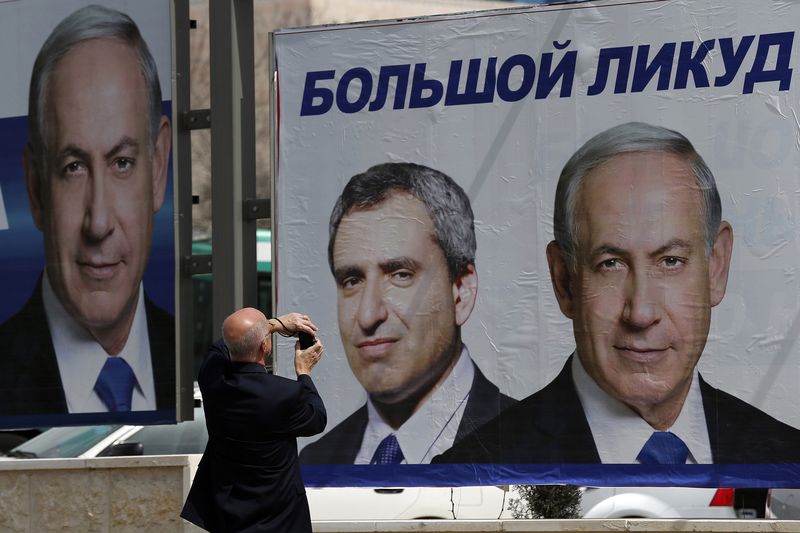 © Reuters. A man photographs Israeli Prime Minister Netanyahu's election campaign banner in Jerusalem